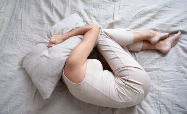 Frightened depressed middle aged woman lying alone on bed in fetal position covering head with pillow feeling afraid or depressed suffer from insomnia mental problem abuse violence concept, top view